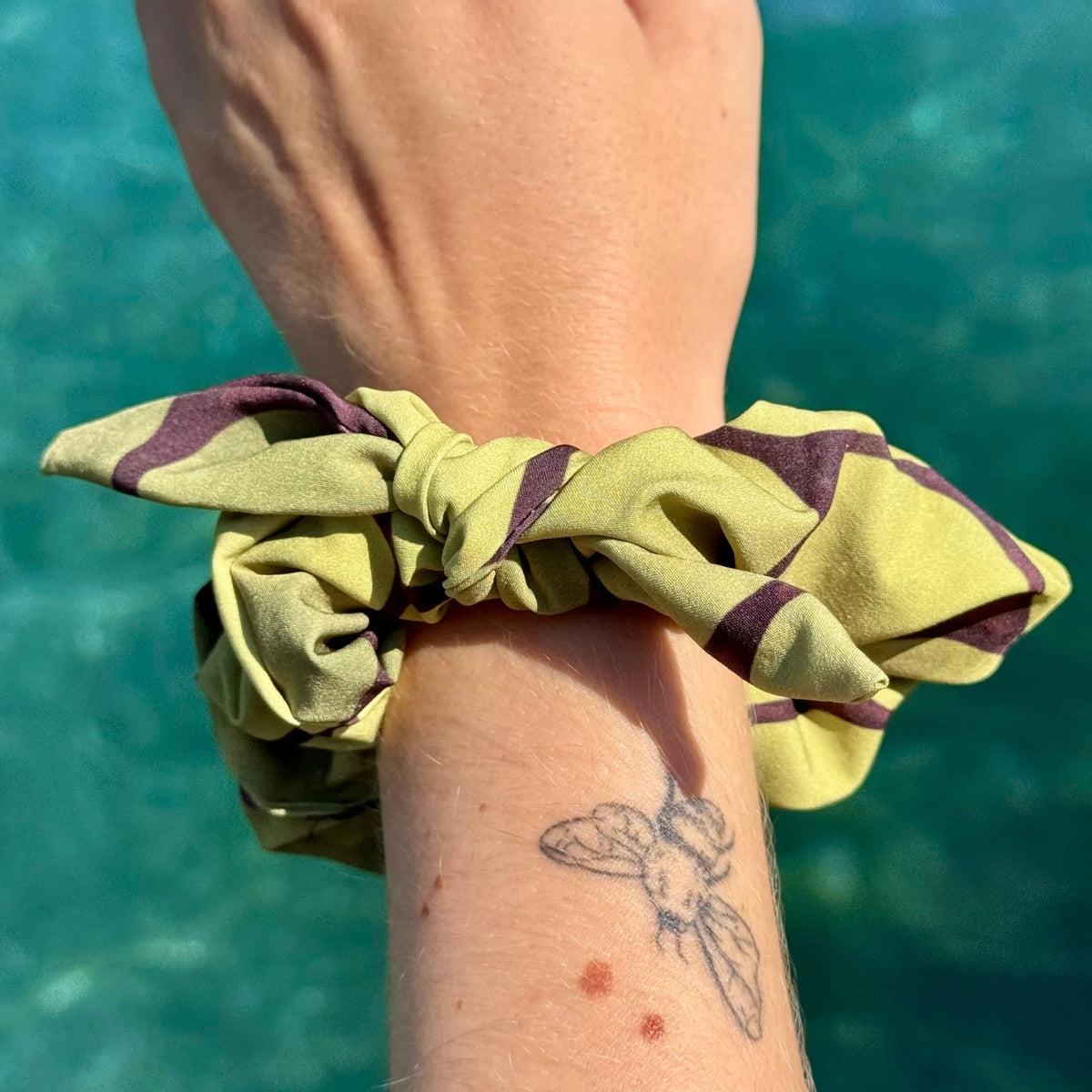 Wrist wearing the Sea Turtle recycled scrunchie over sunlit sea water